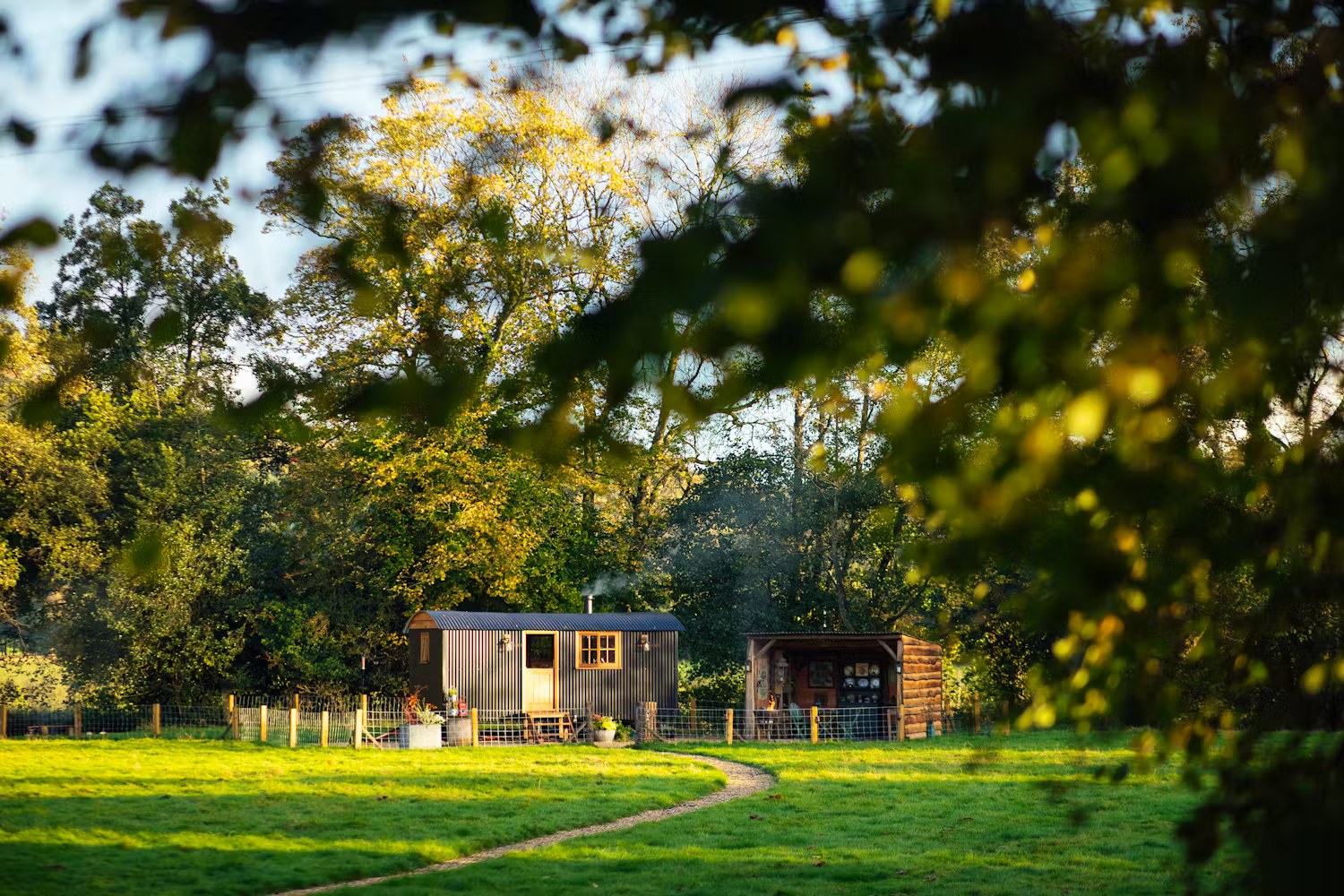 The whole of Millie the Hut and its outdoor shelter, nestled beside trees at the end of a meadow path